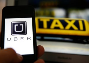 File illustration picture showing the logo of car-sharing service app Uber on a smartphone next to the picture of an official German taxi sign in Frankfurt, September 15, 2014. A Frankfurt court earlier this month instituted a temporary injunction against Uber from offering car-sharing services across Germany. San Francisco-based Uber, which allows users to summon taxi-like services on their smartphones, offers two main services, Uber, its classic low-cost, limousine pick-up service, and Uberpop, a newer ride-sharing service, which connects private drivers to passengers - an established practice in Germany that nonetheless operates in a legal grey area of rules governing commercial transportation.    REUTERS/Kai Pfaffenbach/Files  (GERMANY - Tags: BUSINESS EMPLOYMENT CRIME LAW TRANSPORT)